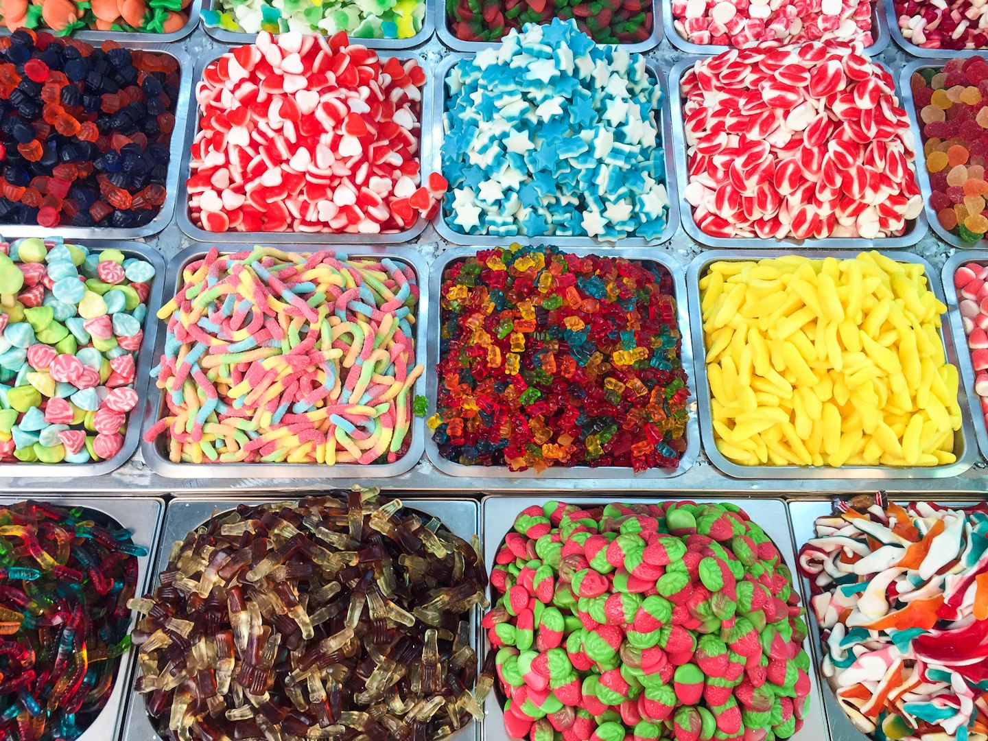 Metal trays overflowing with colorful gummy candies in many shapes.