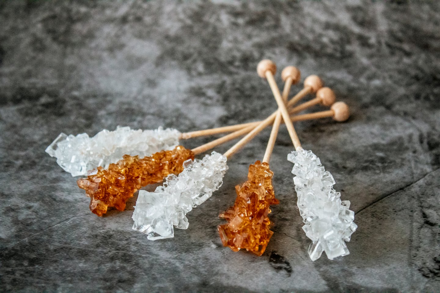 Clear and amber rock candy sticks arranged on textured stone.