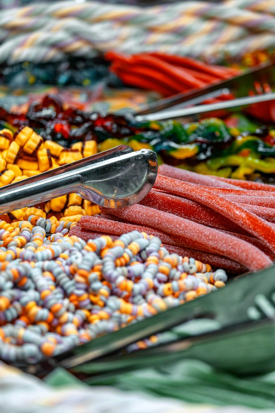 Metal tongs picking up assorted colorful gummy and beaded candies.