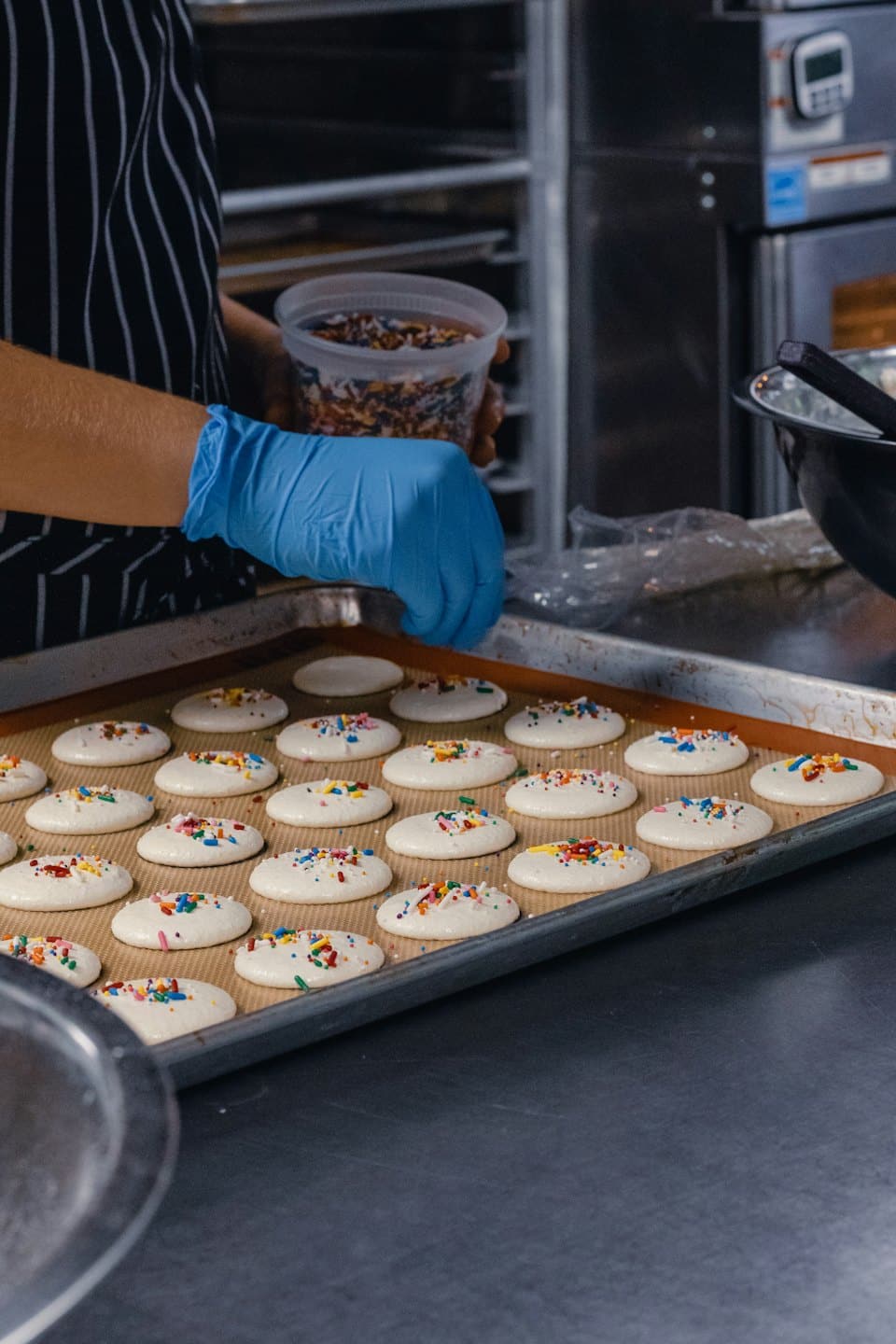 Baker in a striped apron sprinkles candy onto unbaked cookies.