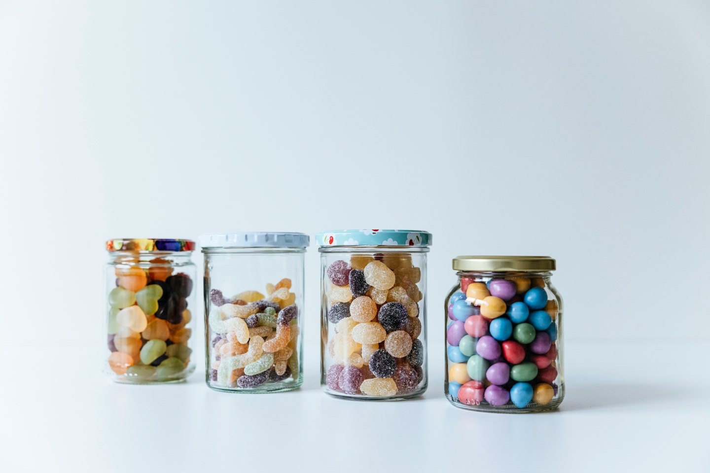 Four glass jars filled with assorted candies sit in a row.