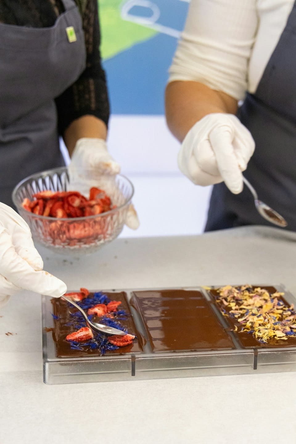 Confectioners carefully decorate chocolate bars with fresh strawberries and petals.