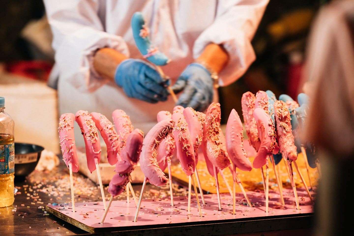 Vendor in a lab coat prepares a candy-coated banana.