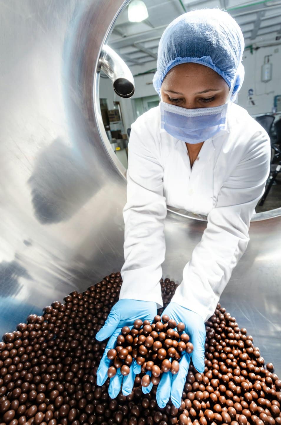 Food worker checking chocolate candies on a production line.